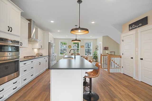 2055 Eva Pearl Dr, Apex, NC 27502 - kitchen with stainless steel appliances, wall chimney range hood, dark wood-style floors, dark countertops, and a breakfast bar area