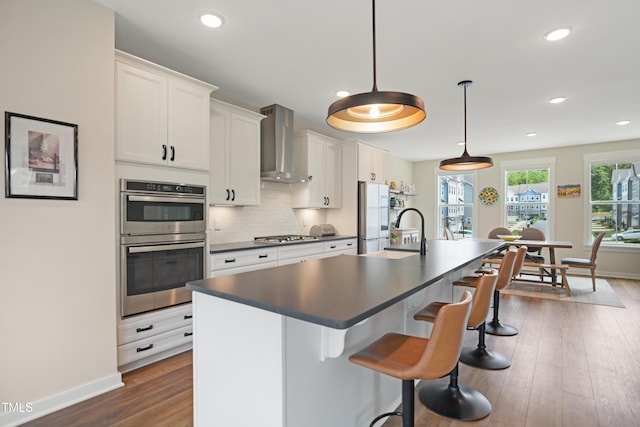 2055 Eva Pearl Dr, Apex, NC 27502 - kitchen featuring wall chimney range hood, dark countertops, stainless steel double oven, freestanding refrigerator, and a kitchen island with sink