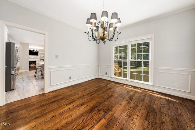 3811 Cottonwood Dr, Durham, NC 27705 - unfurnished room with a chandelier, ornamental molding, a warm lit fireplace, a wainscoted wall, and wood finished floors