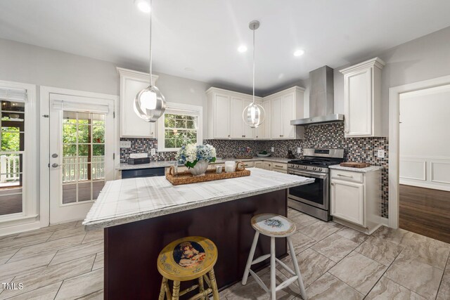 3811 Cottonwood Dr, Durham, NC 27705 - kitchen with stainless steel range with gas stovetop, wall chimney exhaust hood, a kitchen bar, and white cabinetry
