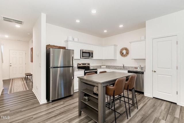 2050 Trailside Dr, Durham, NC 27704 - kitchen with appliances with stainless steel finishes, light wood finished floors, white cabinetry, recessed lighting, and light stone counters