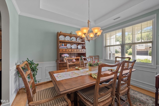 5216 Marcella Ct, Durham, NC 27707 - dining space with a chandelier, arched walkways, a raised ceiling, light wood finished floors, and a wainscoted wall