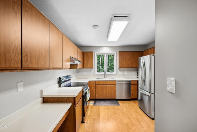 113 Twisted Oak Pl, Durham, NC 27705 - kitchen featuring appliances with stainless steel finishes, under cabinet range hood, light wood finished floors, brown cabinets, and light countertops