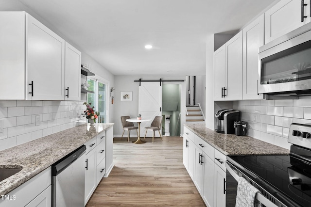 5400 Kaplan Dr, Raleigh, NC 27606 - kitchen featuring appliances with stainless steel finishes, a barn door, white cabinets, light wood finished floors, and recessed lighting