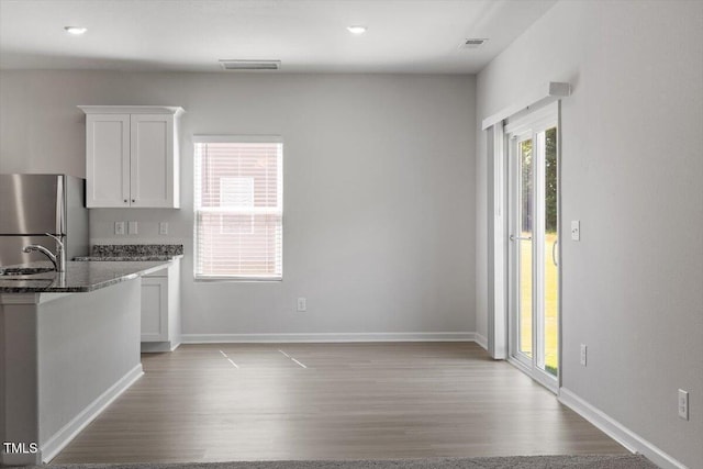 154 Taverners Ln, Angier, NC 27501 - kitchen with freestanding refrigerator, white cabinetry, light wood-style floors, and dark stone counters