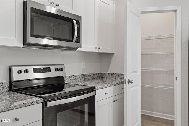 154 Taverners Ln, Angier, NC 27501 - kitchen with stainless steel appliances, white cabinetry, light stone countertops, and wood finished floors