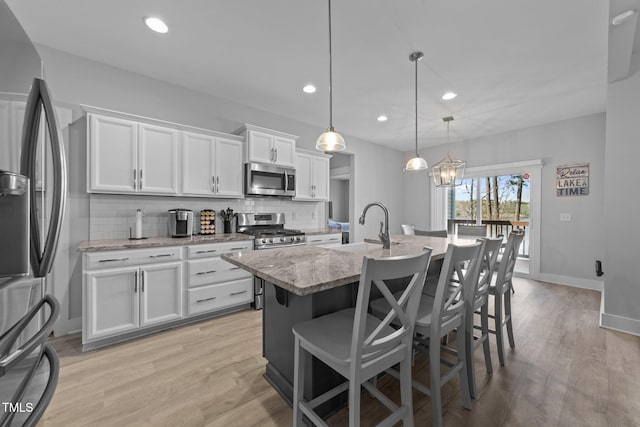 1013 Sagamore Dr, Louisburg, NC 27549 - kitchen featuring appliances with stainless steel finishes, tasteful backsplash, an island with sink, white cabinetry, and light stone countertops