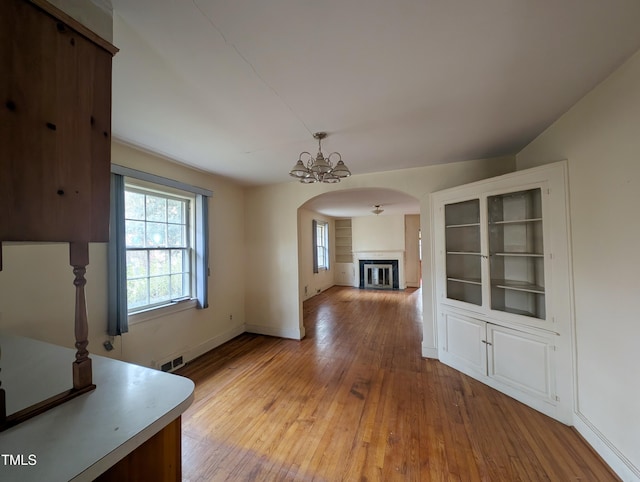 2705 Royster St, Raleigh, NC 27608 - unfurnished dining area with arched walkways, light wood-style floors, a glass covered fireplace, and a chandelier