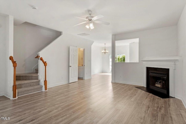 8326 Glenwood Springs Ct, Raleigh, NC 27616 - unfurnished living room with wood finished floors, a chandelier, a ceiling fan, stairs, and a fireplace with raised hearth