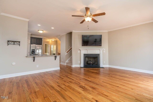 996 Tender Dr, Apex, NC 27502 - unfurnished living room with ornamental molding, light wood finished floors, ceiling fan, stairway, and a fireplace with flush hearth