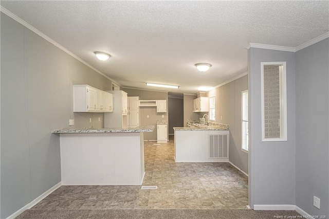 2990 Aberdeen Rd, Raeford, NC 28376 - kitchen with a peninsula, ornamental molding, white cabinetry, a textured ceiling, and light stone countertops