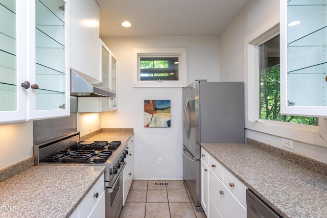 820 Runnymede Rd, Raleigh, NC 27607 - kitchen featuring appliances with stainless steel finishes, wall chimney range hood, white cabinets, glass insert cabinets, and light tile patterned floors