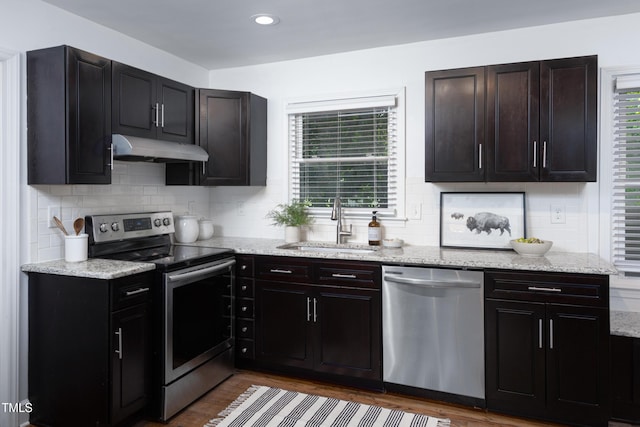 2801 E Shoreham St, Durham, NC 27707 - kitchen with appliances with stainless steel finishes, under cabinet range hood, wood finished floors, tasteful backsplash, and light stone countertops