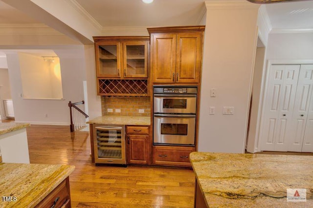 332 Bridgegate Dr, Cary, NC 27519 - kitchen with wine cooler, stainless steel double oven, light wood-type flooring, brown cabinets, and light stone countertops