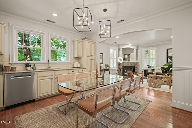 211 W Trinity Ave, Durham, NC 27701 - dining room with a brick fireplace, ornamental molding, light wood-style floors, a chandelier, and arched walkways
