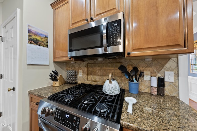 2027 River Grove Ln, Knightdale, NC 27545 - kitchen with stainless steel appliances, backsplash, dark stone counters, and brown cabinetry