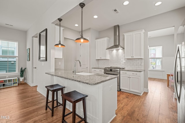 1006 Whistler St, Durham, NC 27713 - kitchen with appliances with stainless steel finishes, wall chimney exhaust hood, a kitchen bar, white cabinetry, and light wood-style flooring