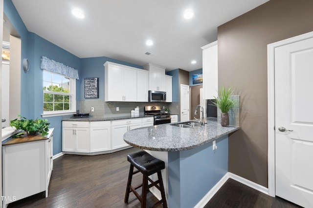 605 Smallwood Dr, Durham, NC 27703 - kitchen featuring stainless steel appliances, a peninsula, a kitchen bar, white cabinets, and dark wood-style floors