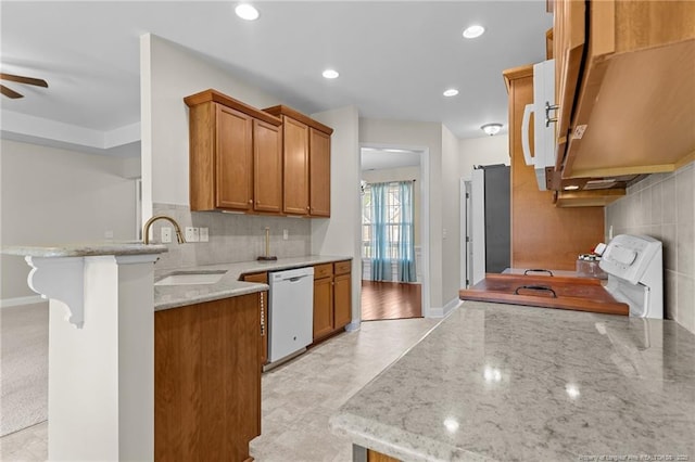 4817 Kiara Dr, Hope Mills, NC 28348 - kitchen featuring white appliances, brown cabinetry, a peninsula, light stone countertops, and decorative backsplash