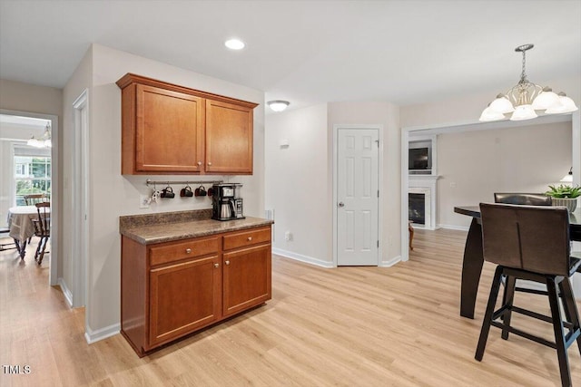 161 Jacob St, Holly Springs, NC 27540 - kitchen with a chandelier, brown cabinets, light wood finished floors, a fireplace, and decorative light fixtures