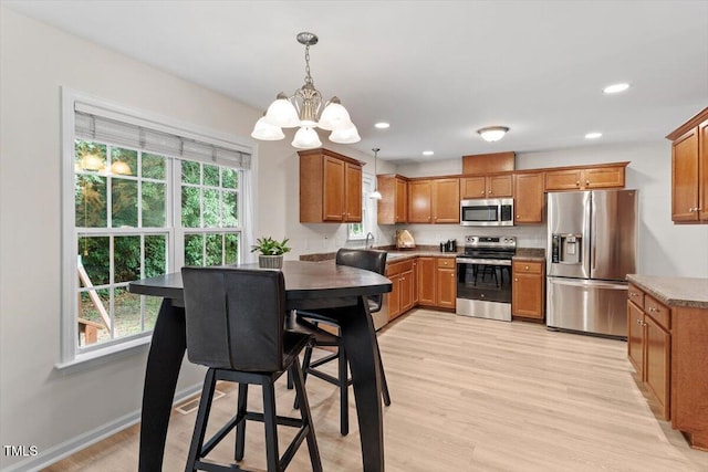 161 Jacob St, Holly Springs, NC 27540 - kitchen with stainless steel appliances, a chandelier, brown cabinets, light wood-style floors, and recessed lighting