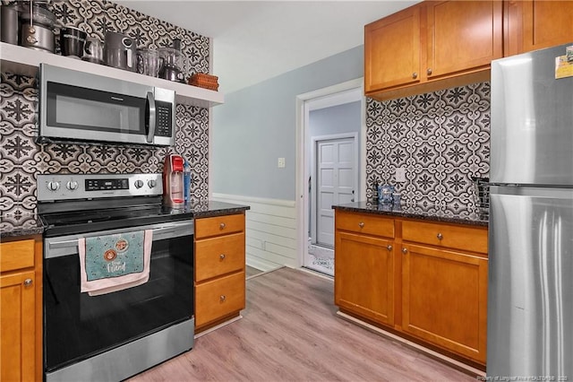 6501 Senator Dr, Fayetteville, NC 28304 - kitchen featuring appliances with stainless steel finishes, light wood-style floors, wainscoting, dark stone counters, and brown cabinetry