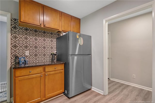 6501 Senator Dr, Fayetteville, NC 28304 - kitchen featuring freestanding refrigerator, light wood finished floors, dark stone countertops, and brown cabinetry