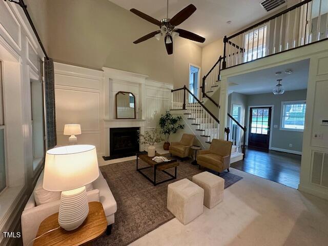 1113 Bexley Hills Bnd, Apex, NC 27502 - carpeted living area with a high ceiling, stairway, a ceiling fan, and a fireplace with flush hearth