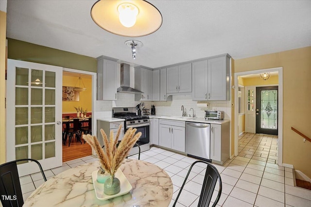 619 Ashe Ave, Cary, NC 27511 - kitchen featuring appliances with stainless steel finishes, wall chimney exhaust hood, gray cabinets, tasteful backsplash, and light countertops