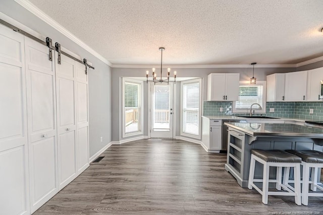 4101 Carson Dr, Sanford, NC 27332 - kitchen featuring a textured ceiling, a barn door, a chandelier, white cabinets, and backsplash