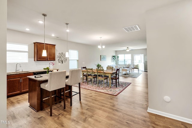 4102 Catfish Way, Durham, NC 27703 - kitchen with a breakfast bar, decorative backsplash, light wood-type flooring, light stone countertops, and decorative light fixtures