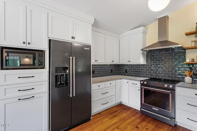 3213 Mid Pines Rd, Raleigh, NC 27606 - kitchen featuring appliances with stainless steel finishes, wall chimney exhaust hood, tasteful backsplash, white cabinets, and light wood finished floors