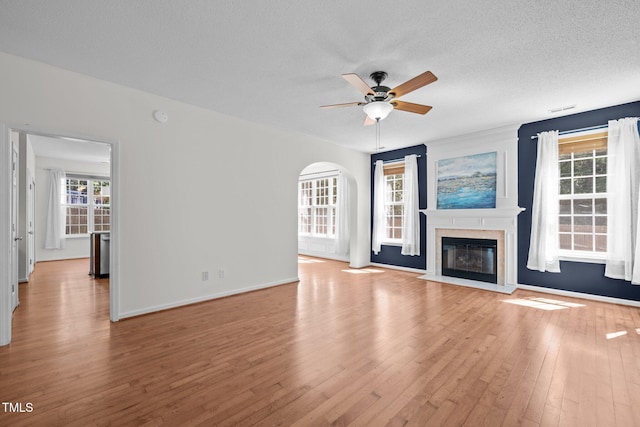 110 Bonhill Ct, Apex, NC 27502 - unfurnished living room with ceiling fan, light wood-style flooring, a glass covered fireplace, a textured ceiling, and arched walkways