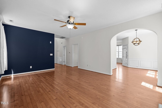 110 Bonhill Ct, Apex, NC 27502 - empty room with arched walkways, ceiling fan, light wood-style floors, a chandelier, and wainscoting