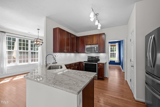 110 Bonhill Ct, Apex, NC 27502 - kitchen featuring stainless steel appliances, a peninsula, light wood-style floors, decorative backsplash, and light stone counters