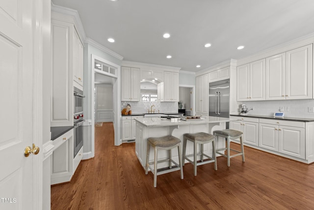 1105 Tazwell Pl, Raleigh, NC 27612 - kitchen with stainless steel appliances, a center island, white cabinetry, tasteful backsplash, and dark wood finished floors