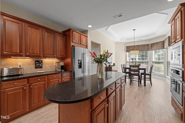 621 Aylestone Dr, Cary, NC 27519 - kitchen featuring stainless steel appliances, a tray ceiling, light wood finished floors, decorative backsplash, and brown cabinetry