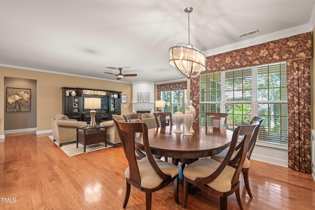 621 Aylestone Dr, Cary, NC 27519 - dining room with crown molding, light wood-style flooring, a chandelier, a fireplace, and a ceiling fan