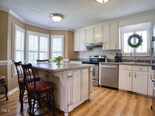 2817 Buckboard Ln, Raleigh, NC 27603 - kitchen featuring appliances with stainless steel finishes, under cabinet range hood, light wood finished floors, a kitchen breakfast bar, and a textured ceiling
