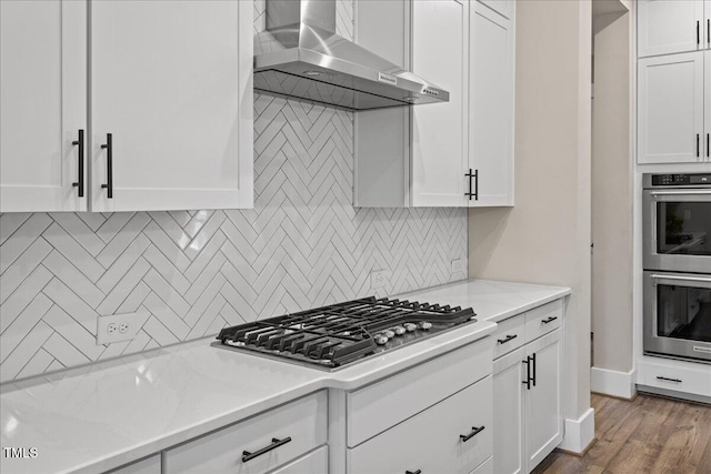 1809 Bowling Rd, Fuquay Varina, NC 27526 - kitchen with wall chimney range hood, appliances with stainless steel finishes, tasteful backsplash, white cabinets, and wood finished floors