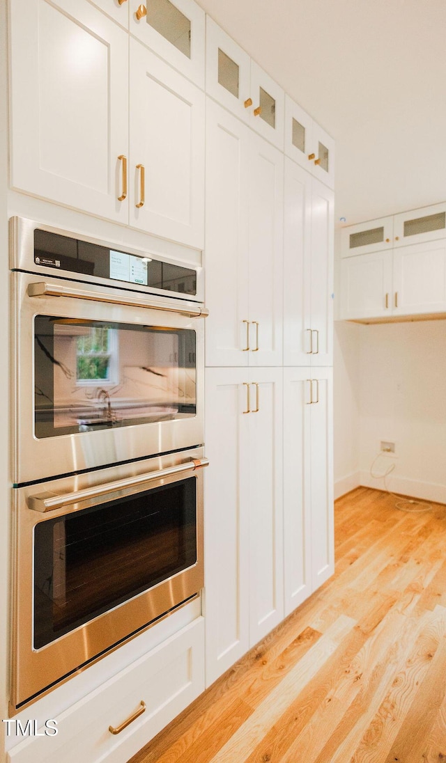 415 E Lavender Ave, Durham, NC 27704 - kitchen featuring double oven, light wood-type flooring, white cabinetry, and glass insert cabinets