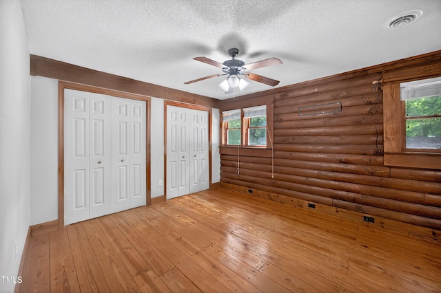 3263 S Jim Minor Rd, Haw River, NC 27258 - unfurnished bedroom featuring rustic walls, a textured ceiling, multiple closets, light wood-style flooring, and ceiling fan