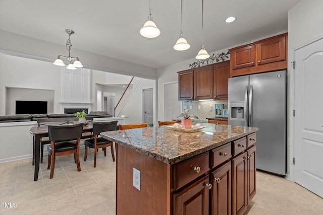 308 Sutton Glen Dr, Apex, NC 27523 - kitchen featuring stainless steel fridge, dark stone counters, a center island, decorative light fixtures, and a fireplace