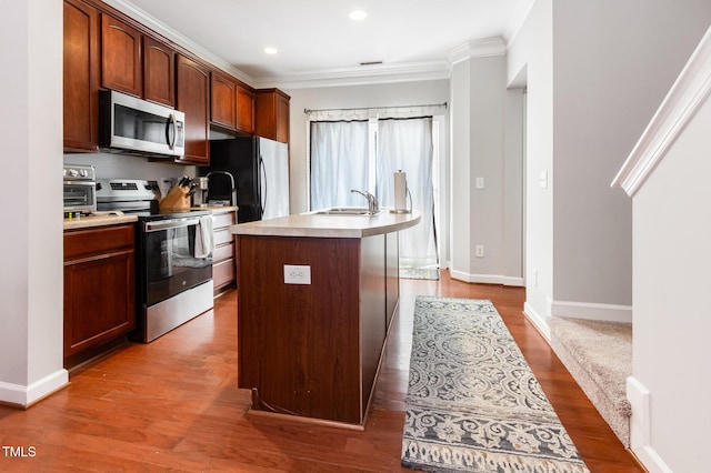8823 Orchard Grove Way, Raleigh, NC 27612 - kitchen with appliances with stainless steel finishes, light countertops, a center island with sink, wood finished floors, and crown molding