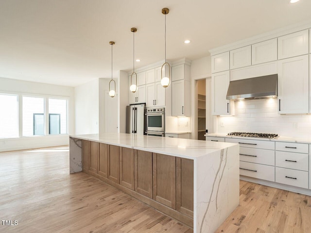 1009 Parker St, Raleigh, NC 27607 - kitchen with wall chimney range hood, appliances with stainless steel finishes, a spacious island, light wood finished floors, and recessed lighting