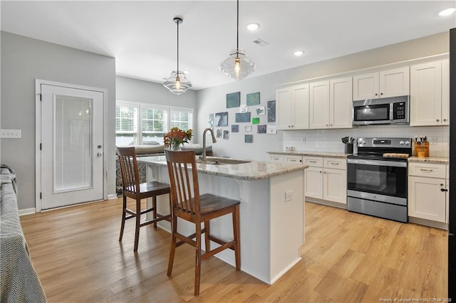 606 N Dickson St, Raeford, NC 28376 - kitchen with stainless steel appliances, a center island with sink, tasteful backsplash, white cabinets, and light wood finished floors