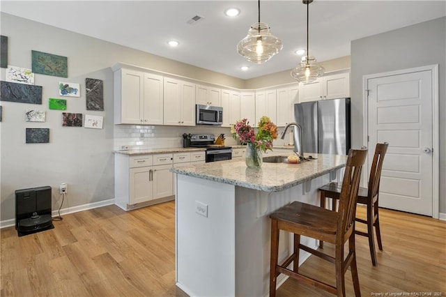 606 N Dickson St, Raeford, NC 28376 - kitchen with stainless steel appliances, a breakfast bar area, light wood-type flooring, white cabinets, and light stone counters