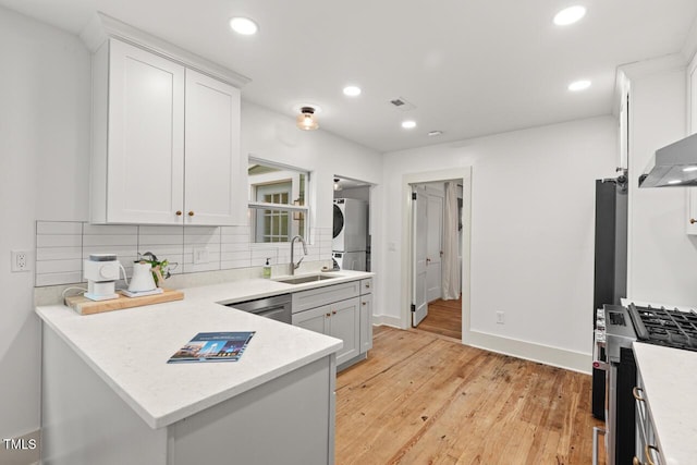 2410 Huron St, Durham, NC 27707 - kitchen with stainless steel appliances, stacked washing machine and dryer, tasteful backsplash, light wood-style flooring, and white cabinetry