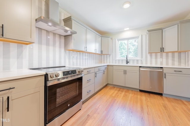 944 Athens Dr, Raleigh, NC 27606 - kitchen with appliances with stainless steel finishes, wall chimney range hood, gray cabinetry, light countertops, and light wood finished floors