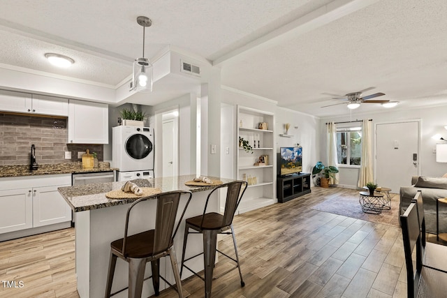 7002 Longstreet Dr Unit C, Raleigh, NC 27615 - kitchen with a textured ceiling, stacked washing machine and dryer, dark stone counters, a kitchen breakfast bar, and crown molding